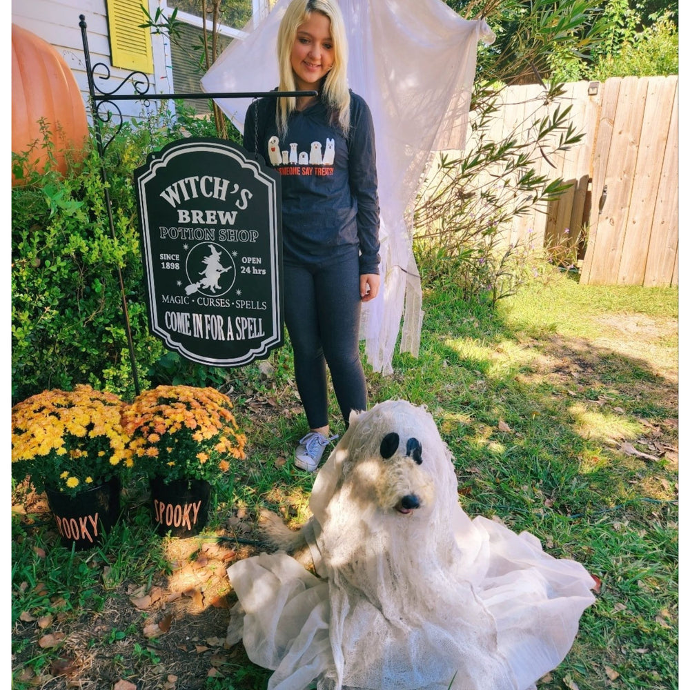 Young woman with her doodle dog in ghost costume. She is wearing a black Halloween Hoodie that features ghostly canines