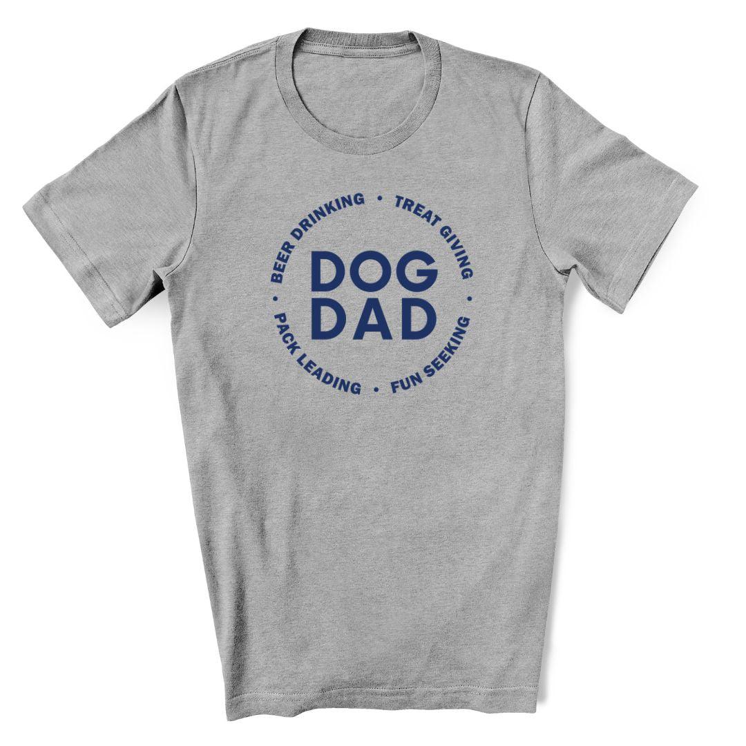 A funny dog dad shirt that is grey with Dog Dad in blue text in the middle and Beer drinking, treat giving, pack leading, fun seeking in blue text featured in a circle around it.